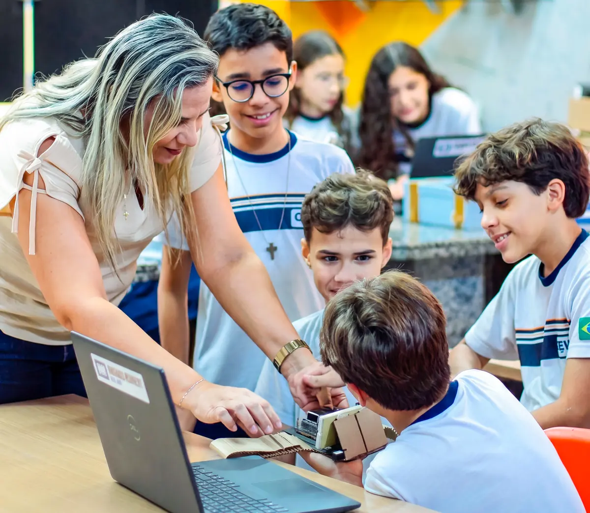 Professora orientando estudantes do CEV Colégio em uma atividade prática com notebook e protótipo